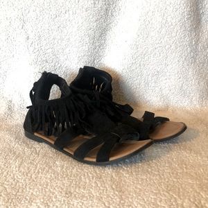 Black flat sandals with fringe around the ankle